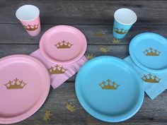 pink and blue plates with gold crowns are sitting on a wooden table next to cups