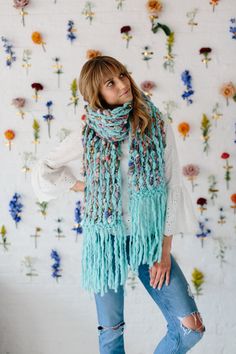 a woman standing in front of a wall with flowers on it and wearing a blue scarf