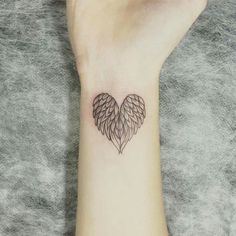 a small tattoo on the wrist of a woman's arm with wings in the shape of a heart