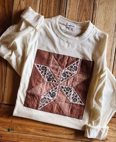 a white shirt with a red and black patchwork design on the front sitting on a wooden floor