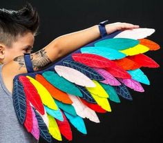 a young man with tattoos on his arm holding a colorful feathered object in front of his face