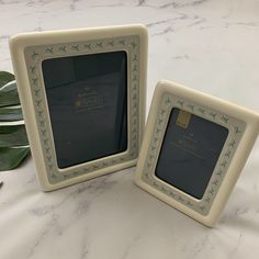 two white frames with green stars on them sitting on a marble counter top next to a plant