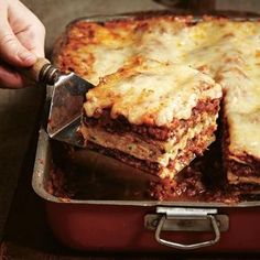 a person cutting into lasagna casserole in a red pan