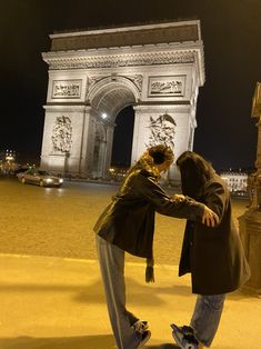 two people standing in front of the arc de trioe at night with their arms around each other