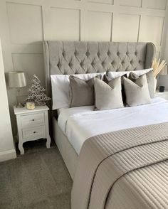 a bed with white linens and gray pillows in a small room next to a night stand