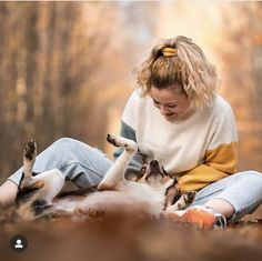 a woman sitting on the ground playing with her dog while it's paw is in the air