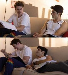 two men are sitting on a couch and one is looking at something in his hand