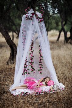 a woman laying on top of a bed covered in pink flowers next to a canopy