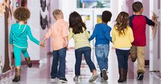 several children are walking down the hallway holding hands and looking at pictures on the wall