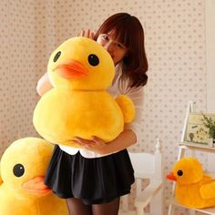 a woman holding two large stuffed ducks in her hands, while standing next to a bed