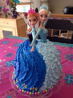 two dolls are sitting on top of a cake