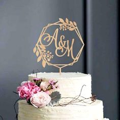 a white cake topped with a gold monogrammed cake topper and pink flowers