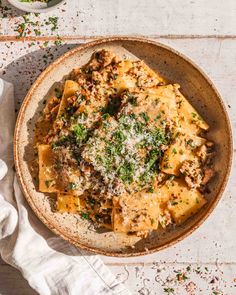 a bowl filled with pasta, meat and parmesan cheese on top of a white table