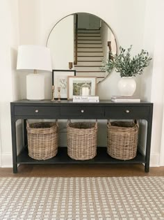 a console table with two baskets on top and a mirror above it, in front of a staircase