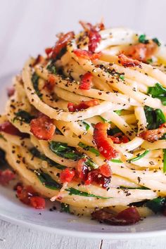 a white plate topped with pasta covered in bacon and spinach sprinkles