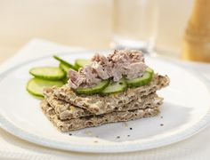 a white plate topped with crackers and cucumbers next to a glass of water