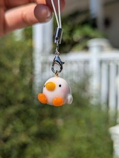 a hand holding a small white and orange pig charm on a chain with an orange nose