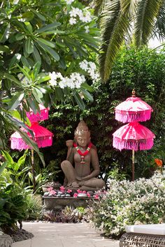 a buddha statue sitting under pink umbrellas in a garden