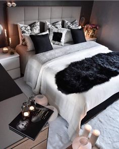 a white bed topped with black pillows next to a night stand filled with lit candles