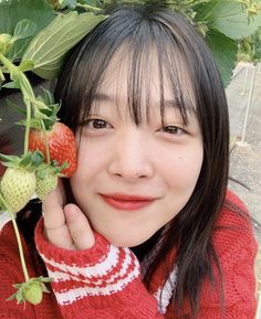 a young woman holding up a strawberry to her face