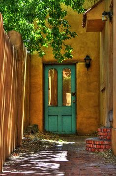 a green door is on the side of a yellow building with a brick path leading to it