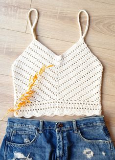 a white crop top and jean shorts on a wooden floor with an orange flower in the middle