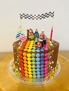 a birthday cake decorated with cars and flags on top of a wooden table in front of a white wall