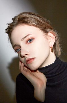 a woman with blue eyes wearing a black turtle neck top and gold hoop earrings, posing for the camera