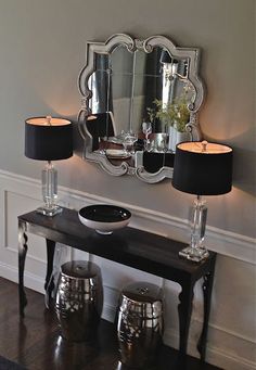 a black table with two lamps and a mirror on the wall above it in a living room