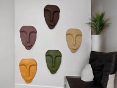 four different colored masks are on the wall next to a chair and potted plant