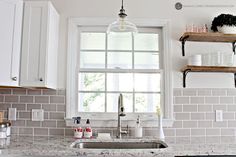 a kitchen sink under a window next to a shelf with cups and glasses on it