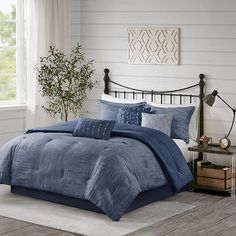 a bed with blue comforters and pillows in a room next to a plant on a table