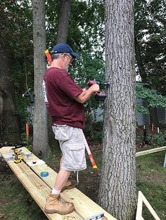 a man standing on top of a wooden bench next to a tree