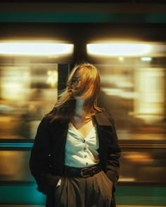 a woman standing in front of a train with her hair blowing in the wind,