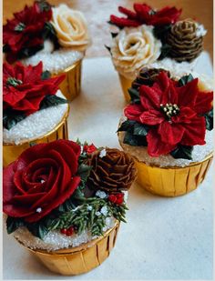 four cupcakes decorated with poinsettia, pine cones and red flowers