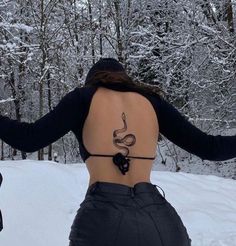 a woman with a tattoo on her back standing in the snow next to some trees