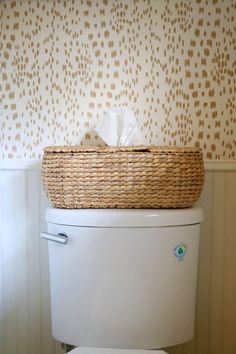 a white toilet sitting next to a basket on top of it's tank cover