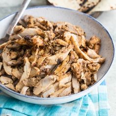 a bowl filled with sliced meat on top of a blue and white towel next to pita bread