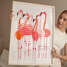 a woman holding up a painting with flamingos on it