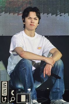 a young man sitting on top of a stage with his arms crossed and legs crossed