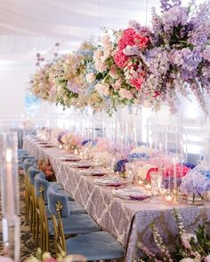 a long table with many flowers hanging from it's ceiling and candles on the tables