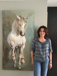 a woman standing next to a painting of a white horse