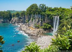 people are swimming in the blue water near a waterfall and some green trees on either side