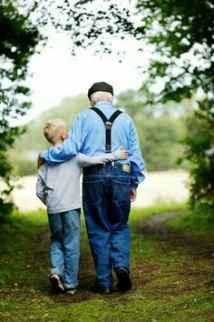 an older man and young boy walking down a dirt path in the woods with their backs to each other