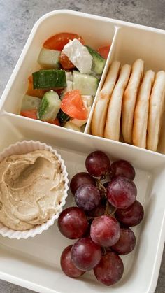 grapes, cucumber, crackers and hummus in a white tray on a table