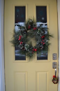 a yellow door with a wreath on it and two windows in the background, all decorated for christmas