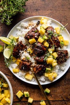 a white plate topped with meat and pineapples next to rice on a wooden table