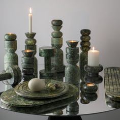 a table topped with candles and rocks on top of a glass table covered in green marble