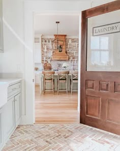 an open door leading to a kitchen and dining room with brick wall, hardwood flooring and white cabinets