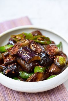 a white bowl filled with cooked vegetables on top of a purple and white table cloth